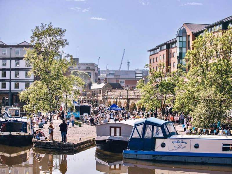A view of Quayside, with people walking along the cobbled streets surrounding the canal. Boats can be seen on the water.