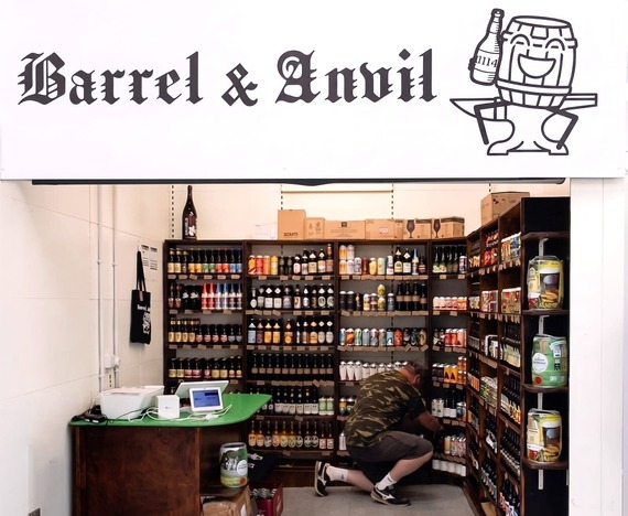 A trader kneels down in a beer stall stocking shelves. The sign above the stall is displayed.