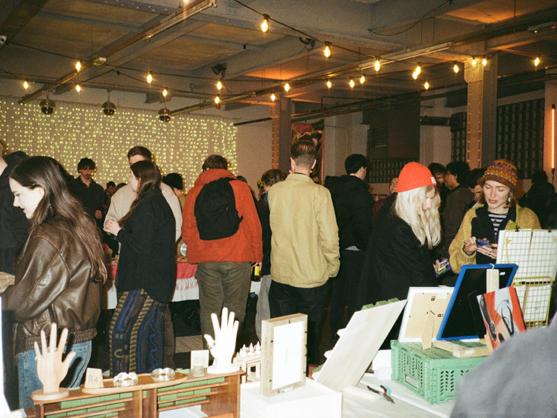 People gathered inside a building, looking at market stalls and conversing with each other.