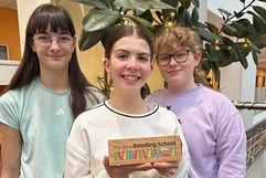 Members of the 'Book Dragons' with their award - three young people smile at the camera holding a reading award plaquard. 