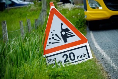 A loose chippings sign on the road verge with works lorries in the background
