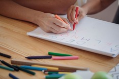 A child's and adults hands, writing letters