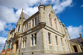 Lerwick Town Hall, a grand stone building with stained glass windows, against a bright blue sky