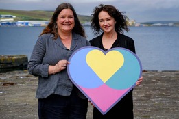 Chief Executive Maggie Sandison and Fiona Duncan of The Promise Scotland, holding the Promise logo in front of the waterfront in lerwick