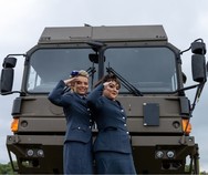 Two women saluting in front of army vehicle