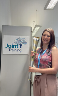 Nicola holding the baton of hope next to a Joint Training poster