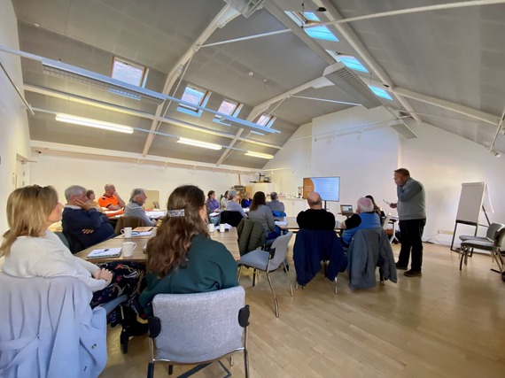 Group of people sat around tables watching a presentation