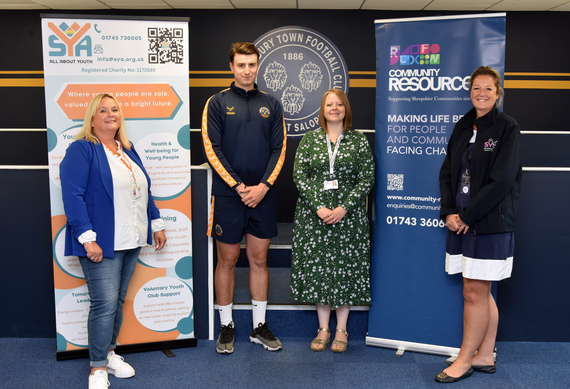 four people stand in front of organisation banners and smile at the camera
