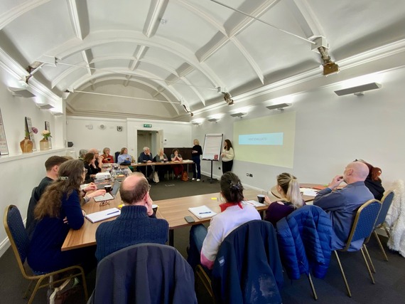 Participants attend a workshop sit in a horseshoe listening to the presenter
