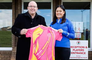 A man and woman hold a football shirt between them and smile at the camera