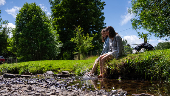 A young girl sits on a grassy bank by a stream