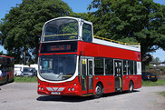 Red and white open top bus in front of some trees