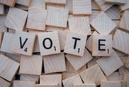 Small wooden letter tiles, the ones on top spell the word vote