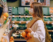 Woman in a fruit and veg shop, she is wearing a face mask and is holding oranges