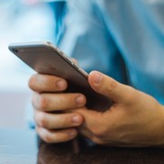 Hands resting on a table holding a mobile phone.