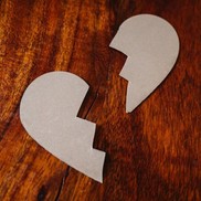 A paper heart broken in two on top of a dark wood surface.