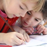 Two young children with heads together drawing with one another.