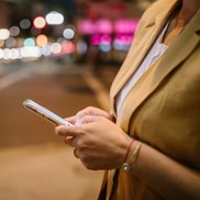 Person stood on the street typing on a mobile phone, there are blurry city lights in the background.