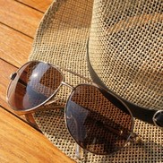Brown sunglasses and a straw hat on a wooden surface.