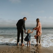 A family on a beach, the man and woman are holding the child's hands as they paddle in the sea.