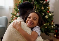 Father and child hugging in front of a Christmas tree.