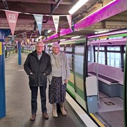 Maggie and Colin Stannard standing in front of pier train lit up pink for Brain Tumour Research.