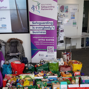 A table full of donated food and other domestic items stored in bags and boxes.