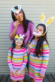 Parent and two children in bright clothes with Easter bunny masks on sticks held up to their faces.