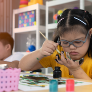 A young girl with Down Syndrome painting in an educational setting.