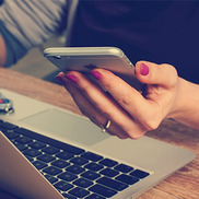 Hand with pink painted nails holding a smartphone next to an open laptop.