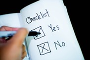 A checklist with yes and no tick boxes with a left hand holding a black ink pen