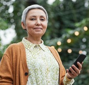 Woman holding her smartphone while smiling at the camera.