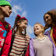 A group of young people of different ethnicities. They are wearing colourful clothes and standing next to each other smiling.