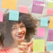 A young woman with curly dark hair behind a transparent board with different coloured post-its