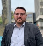 Cllr Daniel Cowan, Leader of the Council a white man in a dark grey suit stood in front of the fountains at the Civic Centre.