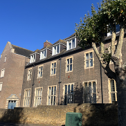 A 3 story school building sits under a blue sky with part of a tree on the right hand side.