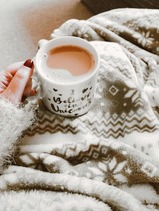 Person under a fleece blanket, they are holding a mug of coffee.