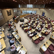 The council chamber with a semi-circular seating arrangement filled with attendees, many using laptops and taking notes.