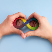 Close up of two hands forming a heart shape and an infinite rainbow symbol within them.