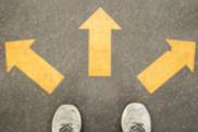 A pair of grey shoes at a crossroads with three yellow arrows pointing forward, left, and right, indicating a decision point.