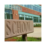 A sign with the text "school". A school building with orange bricks, green panels and window shows behind the sign.