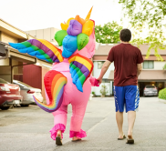 A person dressed up as a colourful unicorn walking away from the camera. There is another person holding their hand.