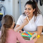 A therapist in a white top helping a girl with speech and language therapies.