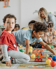 Children playing on a floor mat. There are toys and plastic balls scattered on the floor.