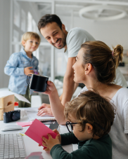 A family of two adults and 2 children in their home office. There are paper on the desk and a PC keyboard. 