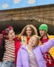 Four young people wearing colourful clothes. They are outdoors and smiling at the camera.