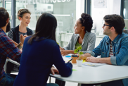 A group of people working together. They are sitting at a table and talking to each other.