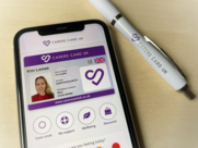 A phone displays the Carers Card UK App, featuring a clear image of the distinctive purple card. Beside the phone rests a branded pen.