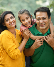  A smiling family of three. A woman in a yellow shirt, a man in a green shirt, and a girl is on the man's back, between the two adults.
