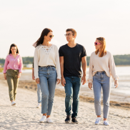 A group of 3 people walking together on a sandy beach. They are talking to each other.